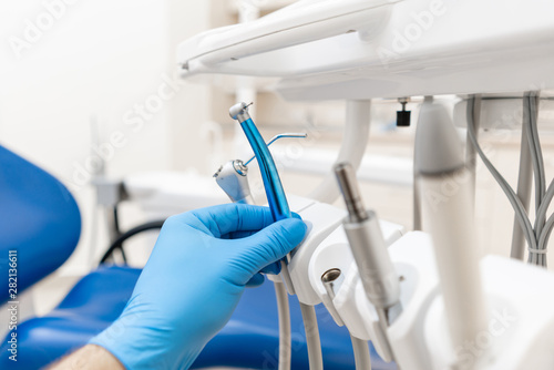 Close-up hand of dentist in the glove holds dental high speed turbine. Office where dentist conducts inspection and concludes.