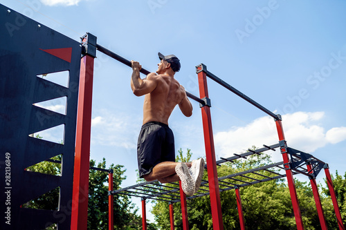 Brutal athletic man making pull-up exercises on a crossbar at outdoor streeet gym.