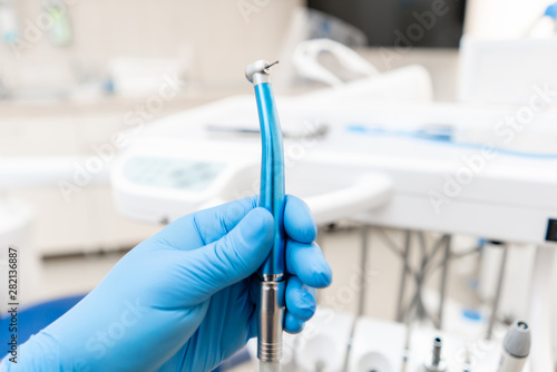 Close-up hand of dentist in the glove holds dental high speed turbine. Office where dentist conducts inspection and concludes.