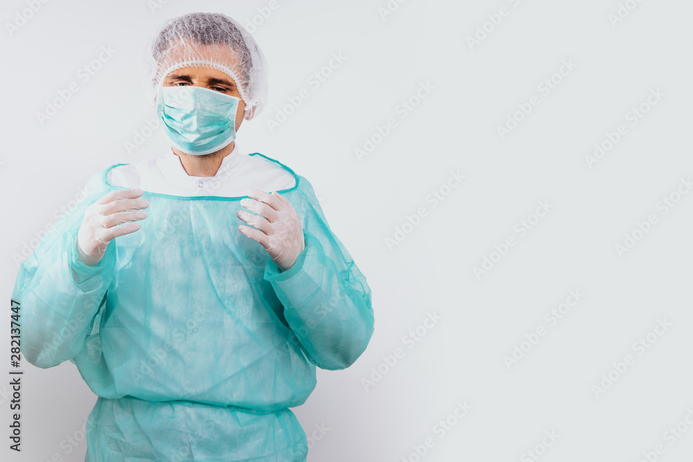 Man dressed in a green surgical apron and a mask on his face on a white background. Medical and pharmaceutical concept. Doctor or surgeon. Preparation for surgery, treatment of people. Man dressed in a green surgical apron and a mask on his face on a white background. Medical and pharmaceutical concept. Doctor or surgeon. Preparation for surgery, treatment of people.