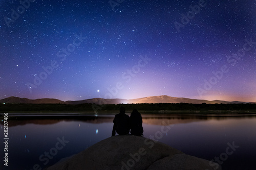 A couple in front of a lake in a starry night