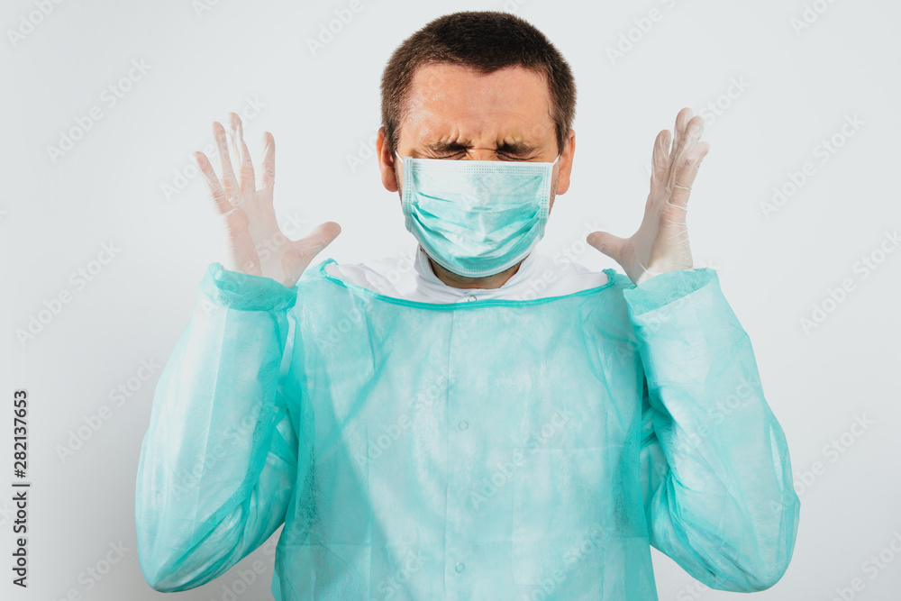 Angry and frustrated surgeon after surgery dressed in a green surgical apron and face mask on a light background. Medical and pharmaceutical concept. Failure of surgery, anger, medical errors.