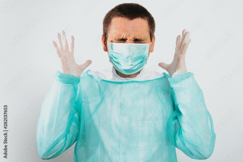 Angry and frustrated surgeon after surgery dressed in a green surgical apron and face mask on a light background. Medical and pharmaceutical concept. Failure of surgery, anger, medical errors. Angry and frustrated surgeon after surgery dressed in a green surgical apron and face mask on a light background. Medical and pharmaceutical concept. Failure of surgery, anger, medical errors.