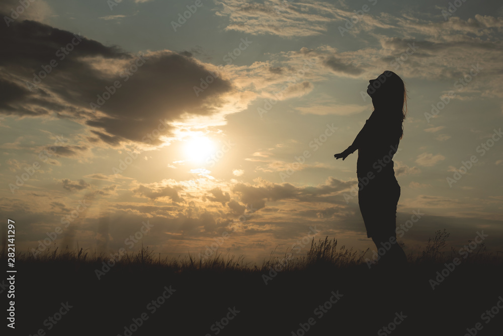 Silhouette of young dreaming woman in a sunset rays.