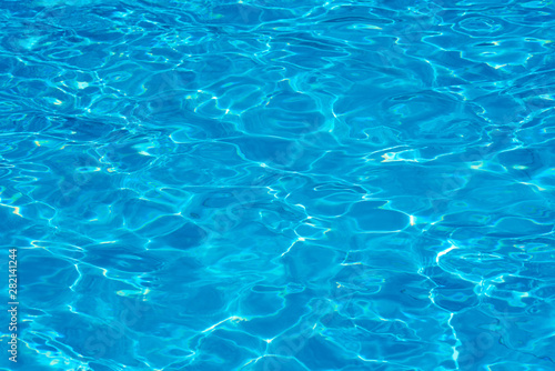Background of water in a blue swimming pool, water surface with sun reflection