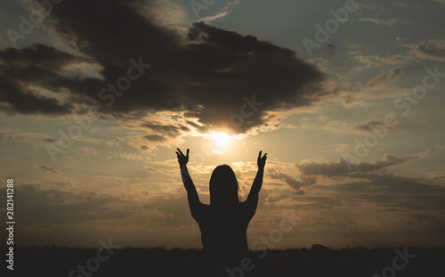 Silhouette of young woman which is looking at a sky in a sunset rays and is stretching her hands to a sun .