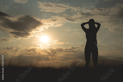 Silhouette of young woman which is looking at a sky in a sunset rays.