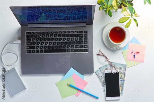 Foto Office workstation with laptop, flower, cup of tea and stationery on white table