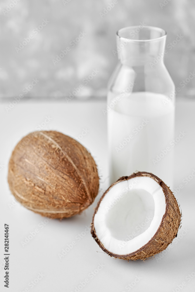 Coconut milk in glass bottle and fresh coconuts with half on a gray background Coconut milk in glass bottle and fresh coconuts with half on a gray background