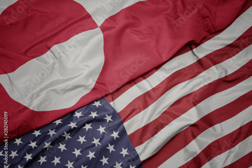 waving colorful flag of united states of america and national flag of greenland.