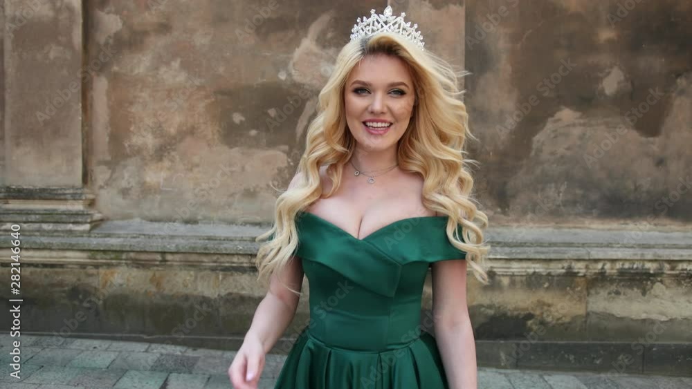 girl, blonde, in a green dress with bare shoulders, with a chic hairstyle and bright make-up, a crown on her head, posing and spinning in front of the camera, a close-up girl, blonde, in a green dress with bare shoulders, with a chic hairstyle and bright make-up, a crown on her head, posing and spinning in front of the camera, a close-up