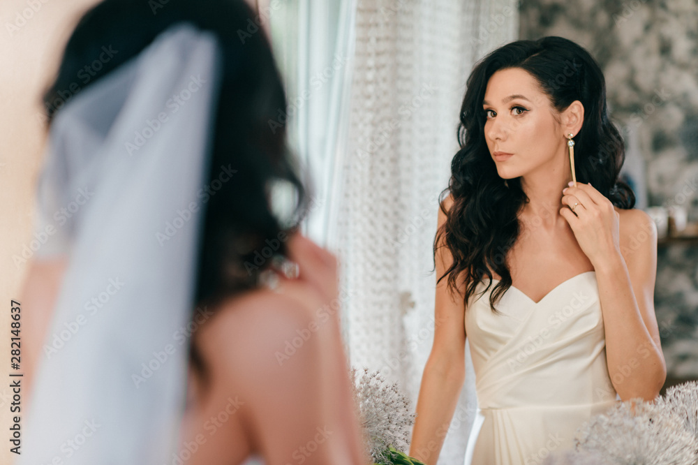 Beautiful young bride in white wedding dress looking in mirror