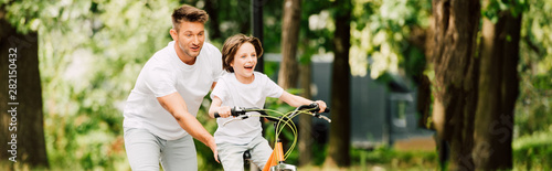 panoramic shot of father pushing bike while son riding bicycle