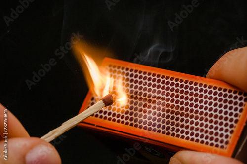 Man's fingers lighting a match, setting fire on friction. On a black background. Matches and fire. Smoke.