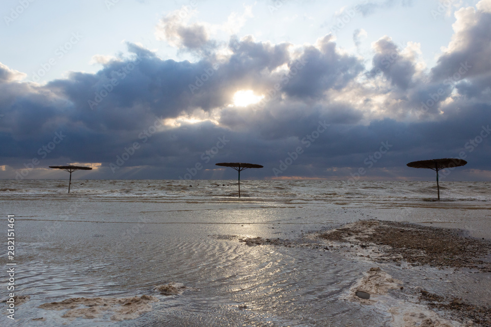 Sea waves flood the beach with beach umbrellas during a storm on the sea on a summer evening at sunset. Sea waves flood the beach with beach umbrellas during a storm on the sea on a summer evening at sunset.