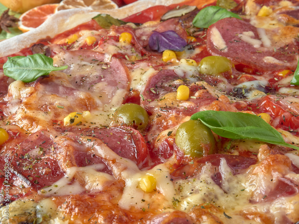 Pizza on thin dough.With slices of salami and ham ,olives and tomatoes.On a background of vegetables. Pizza on thin dough.With slices of salami and ham ,olives and tomatoes.On a background of vegetables.