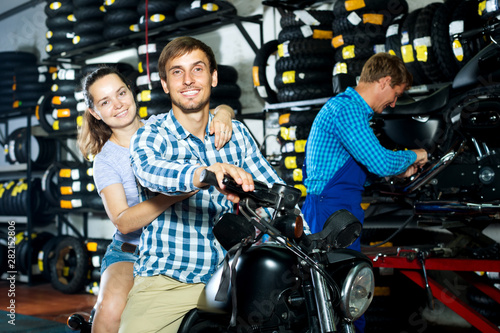 Cheerful couple sitting on motorcycle at service point