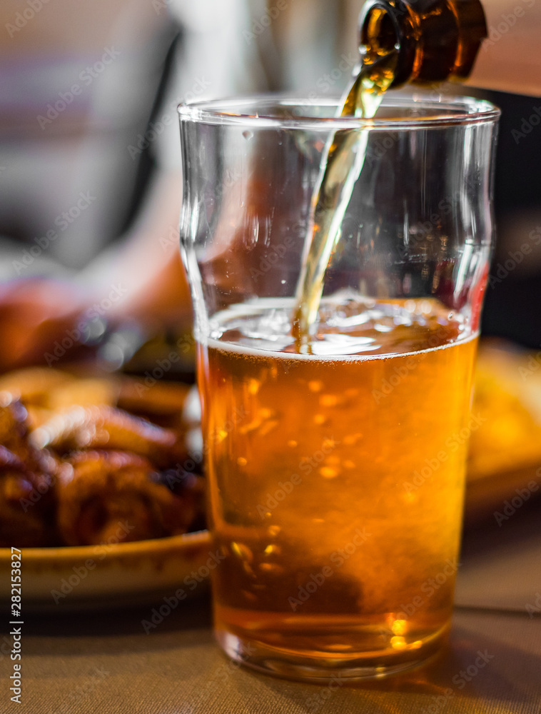 pouring beer in glass from bottle on bar or pub pouring beer in glass from bottle on bar or pub
