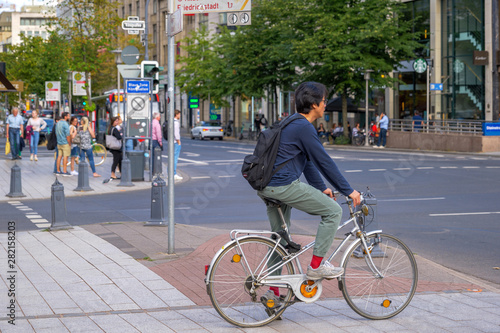 Asian man ride bicycle on the bicycle lanes cross at pedestrian crossing at Königsallee in Düsseldorf, Germany. Cycling and Eco friendly city in Germany. 