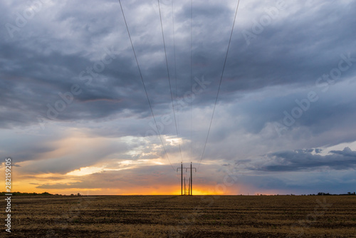 Obraz na płótnie A row of high voltage electrical power lines cling to the horizon in an otherwise vast, wide open rural landscape on sunset with clouds w salonie