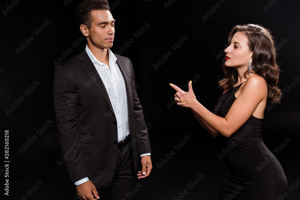 attractive girl pointing with finger at mixed race man isolated on black attractive girl pointing with finger at mixed race man isolated on black