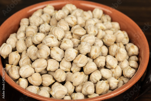 Raw chickpeas in a ceramic bowl on a dark  wooden  background. top center view, out of range.