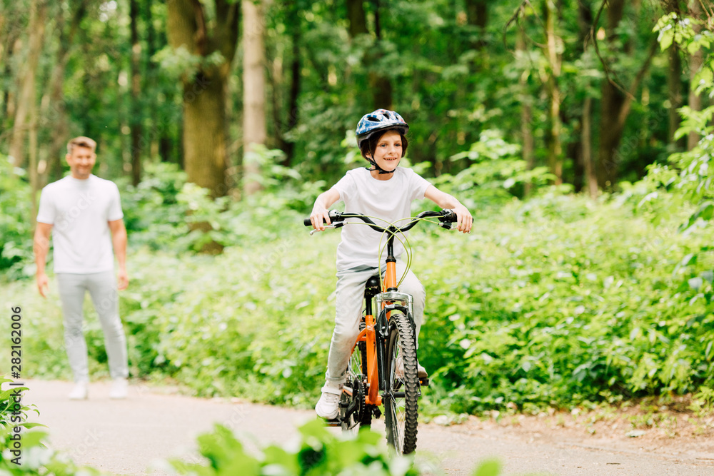 selective focus of happy boy riding bicycle and father standing and looking at son