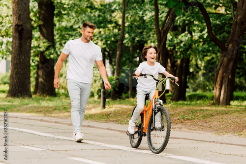 full length view of son riding bicycle while father walking after kid