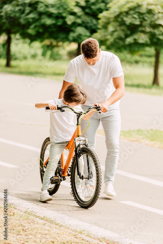 full length view of son trying to sit on bicycle while father holding bike