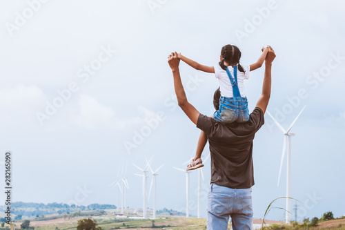 Father and daughter having fun to play together. Asian child girl riding on father s shoulders in the wind turbine field
