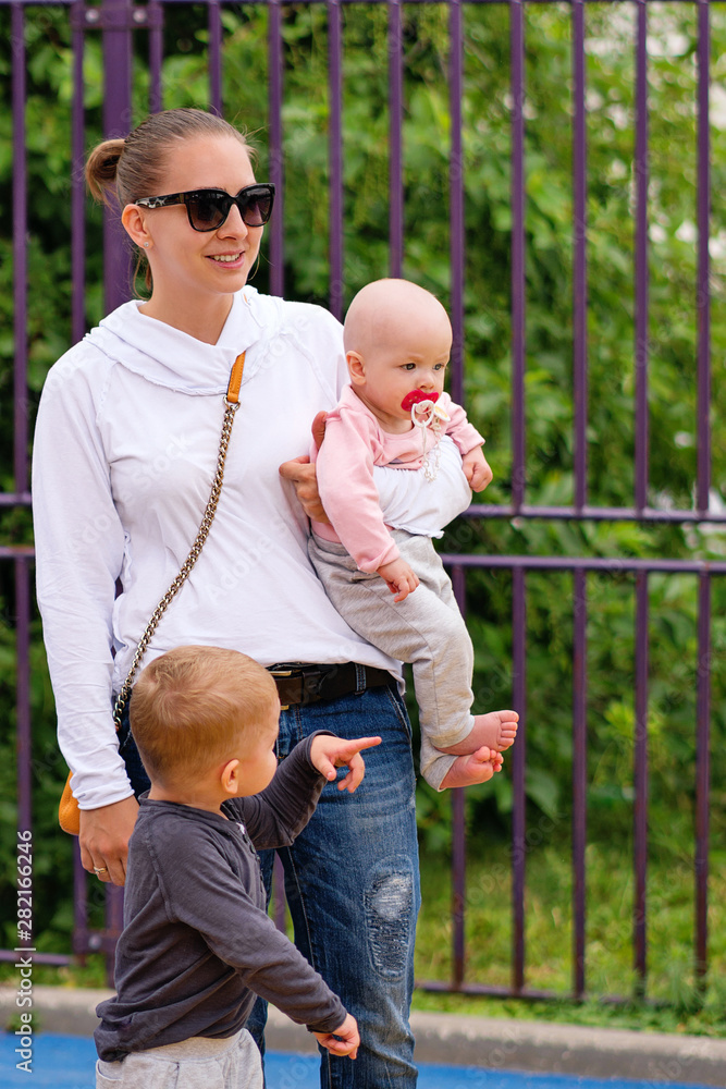 Fototapeta premium Small childrenspend time with mom. Young mother walks with children. Happy family. Young mommy fooling around with a child. Good relations of parent and child. Happy moments together.