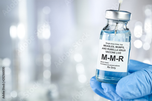 Healthcare concept with a hand in blue medical gloves holding MMR, measles, mumps, and rubella, vaccine vial photo