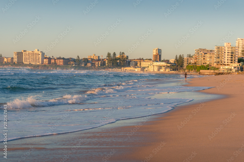 Sunrise beach seascape with unrecognizable surfer and cityscape in the distance