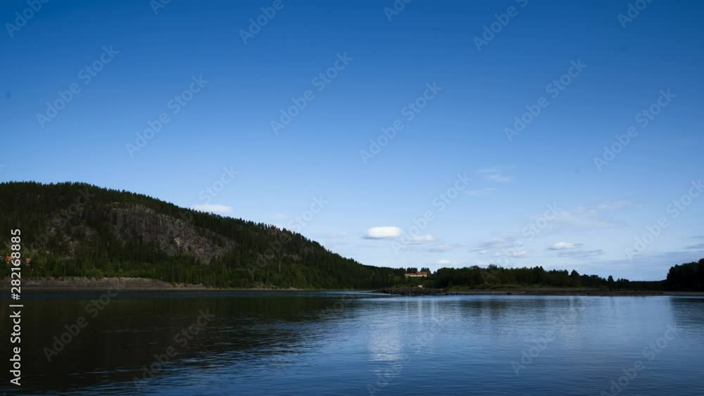 Timelapse of a small mountain with a river in the foreground with a blue summersky.