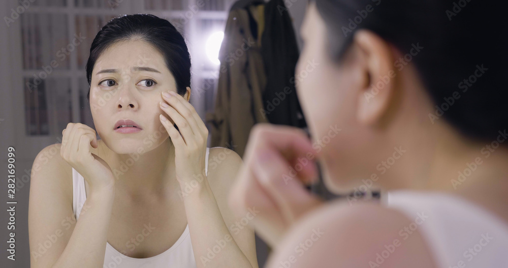 Young asian woman model worrying about her skin. frowning girl looking in mirror of dressing table in backstage. depressed female actress sitting at makeup place examining her face carefully. Young asian woman model worrying about her skin. frowning girl looking in mirror of dressing table in backstage. depressed female actress sitting at makeup place examining her face carefully.