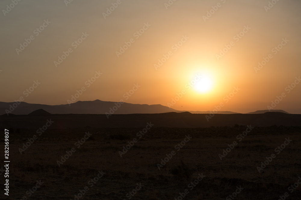 Morning landscape with mountains and orange sky at sunrise with sun reflecting. Evening sunset on the horizon of hills