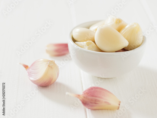 Peeled and unpeeled cloves of garlic on a white wooden table. Component of traditional medicine.