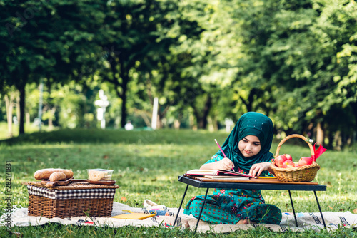 Photography Portrait of happy little muslim girls child with hijab dress smiling and enjoy relax reading and write a book in summer park