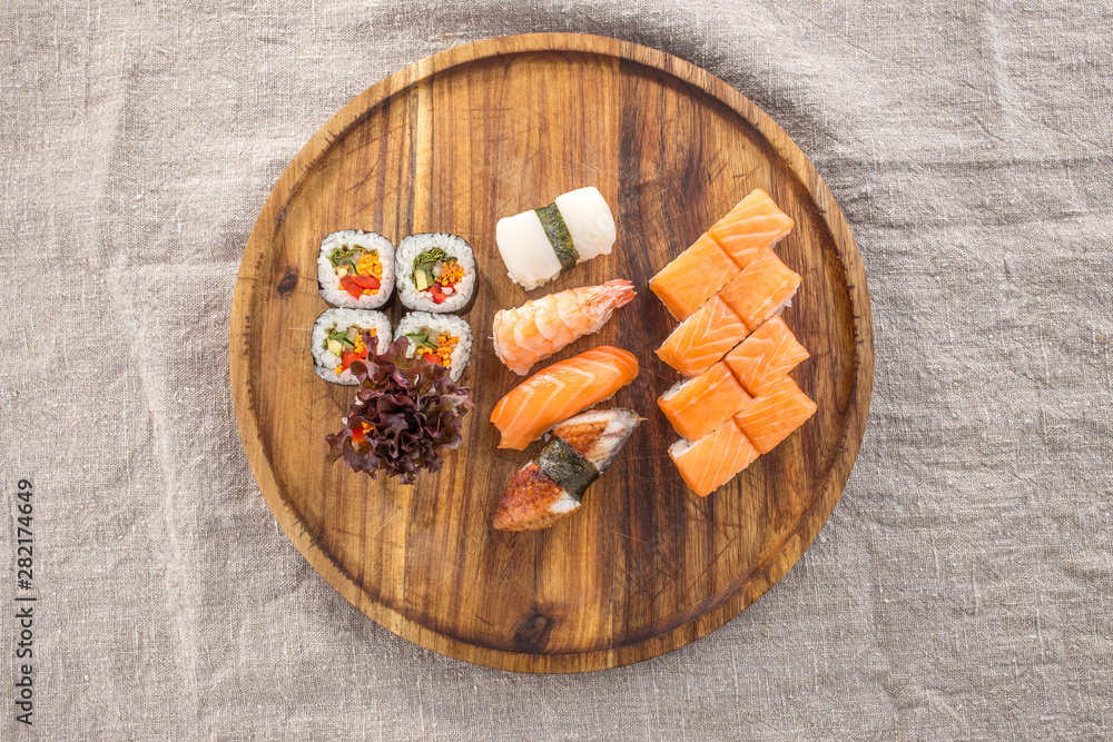 Japanese food restaurant sushi maki roll set on wooden round board on fabric grey background