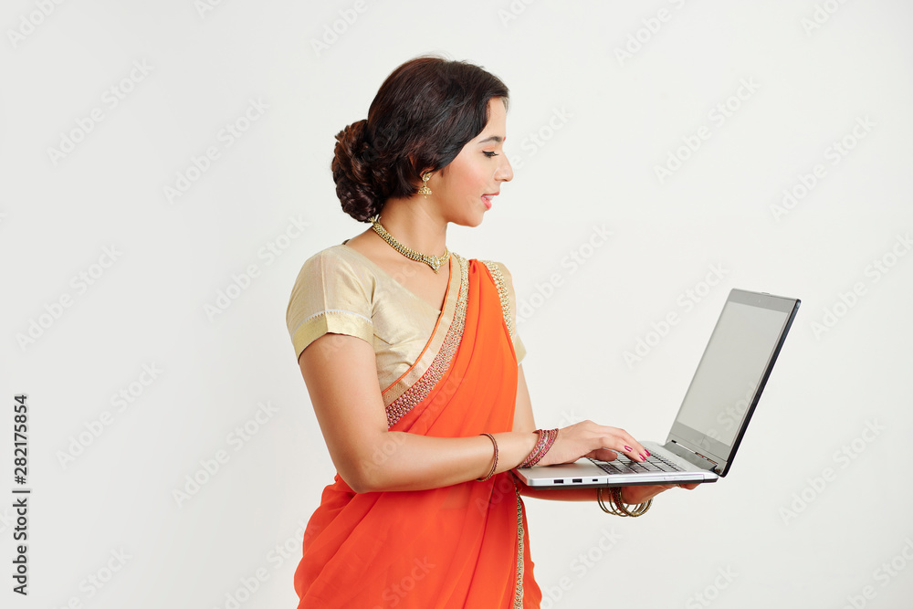 Young Indian woman in traditional orange sari answering e-mails on her laptop, isolated on white Young Indian woman in traditional orange sari answering e-mails on her laptop, isolated on white