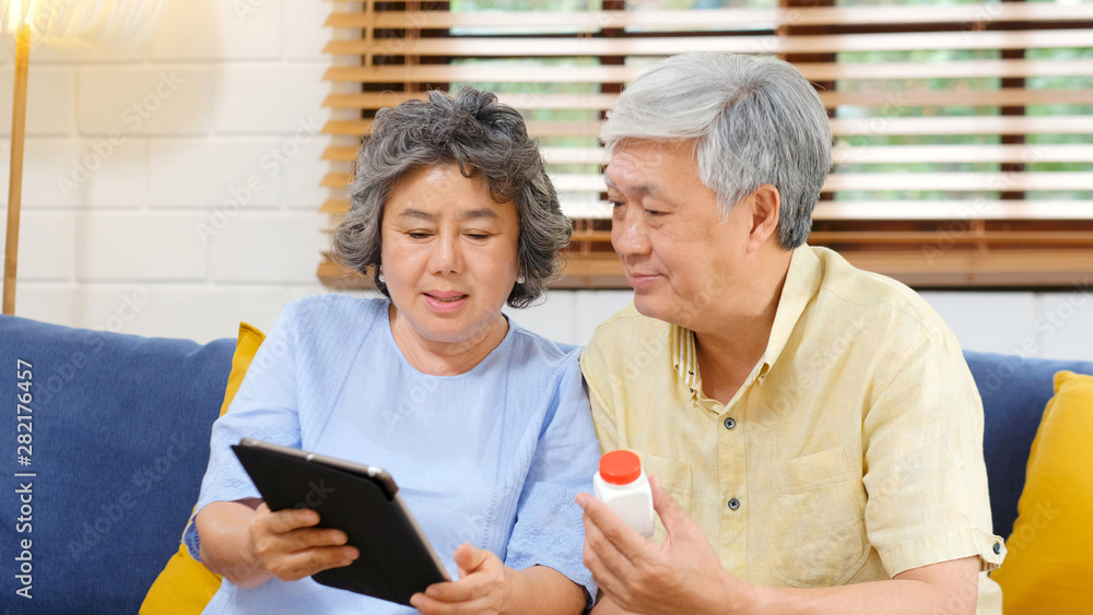 Senior asian couple holding bottle of pill using digital tablet to make video conference call to doctor, pharmacy consulting about medical health care for retirement, old people and technology