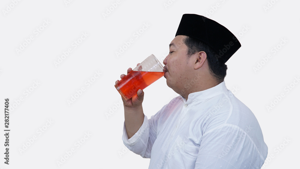 portrait of overweight muslim man with head cap or songkok drink a large glass of tea to break the fast portrait of overweight muslim man with head cap or songkok drink a large glass of tea to break the fast