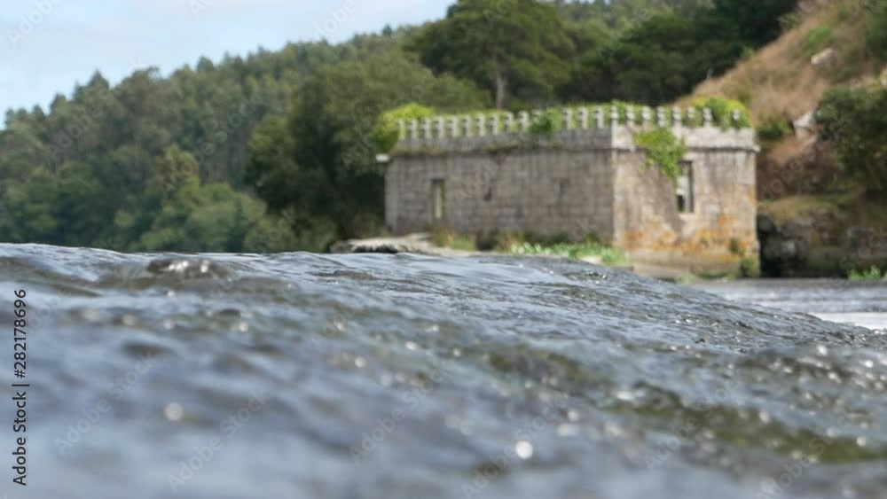 Fresh, clear water running over rocks on Ave River in Portugal with castle ruin in background. Shallow depth of field with focus on water. Fresh, clear water running over rocks on Ave River in Portugal with castle ruin in background. Shallow depth of field with focus on water.