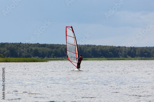 Windsurfing on a Board with a transparent sail riding on the river against the green shore - outdoor activities, extreme water sports