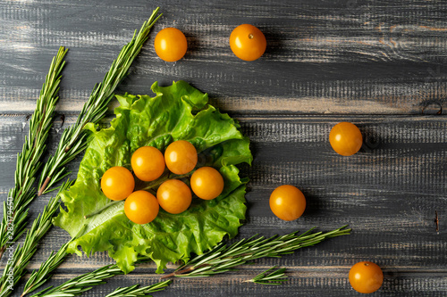 yellow cherry tomato branch on lettuce leaf and rosemary. Vegetables on black wooden table. Copy space.