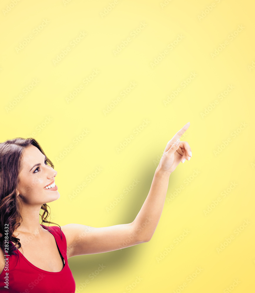 Profile view of smiling young woman in casual red dress, reading and pointing up at copy space, visual imaginary or something, or pressing virtual button. Profile view of smiling young woman in casual red dress, reading and pointing up at copy space, visual imaginary or something, or pressing virtual button.