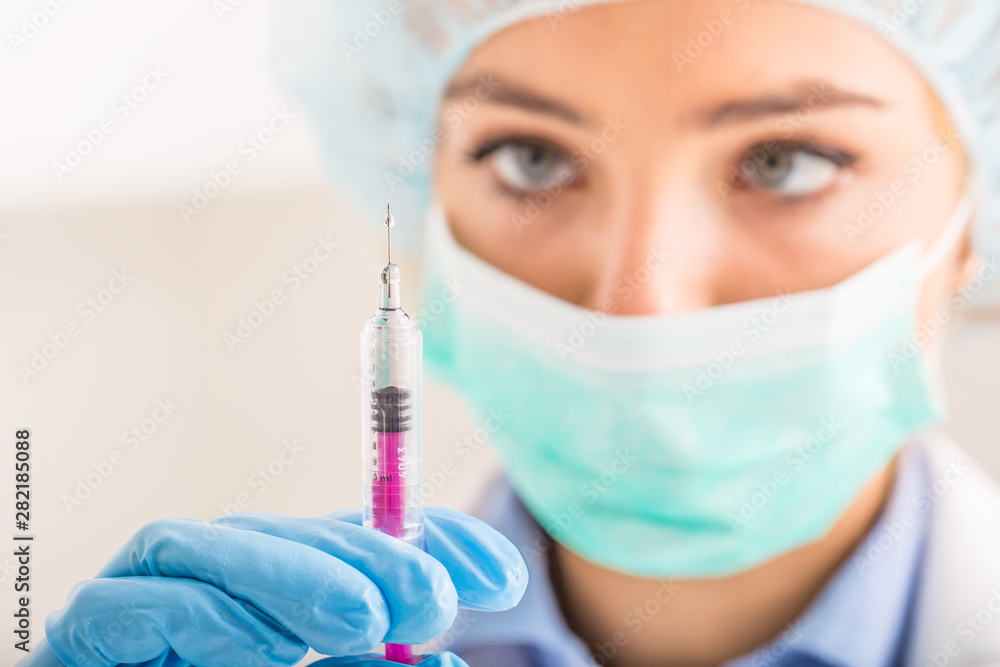 Female doctor working with syringe needle and ampoule of medicine. A scientist in sterile clothes is making a vaccine drug Female doctor working with syringe needle and ampoule of medicine. A scientist in sterile clothes is making a vaccine drug