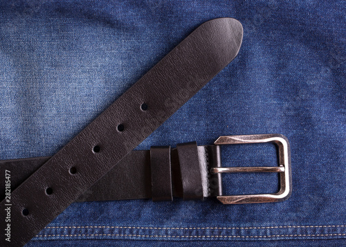 Leather belt lying on jeans. Black leather belt and blue jeans close-up.