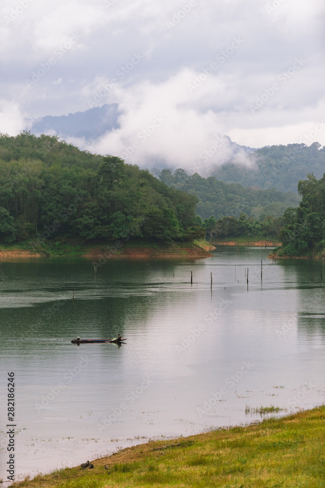 Fisherman and small fishing boat and floating in Bang Lang reservoir in the rain.