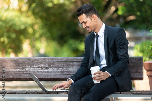 Malay Business man working on his laptop during his coffee break at the park.